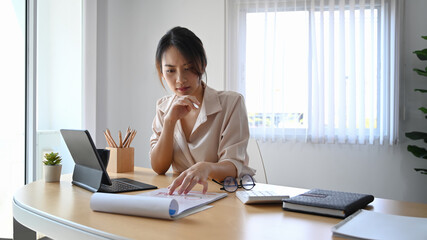 Wall Mural - Young woman accountant analizing business data and working with computer tablet at office desk.