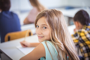 school girl writing on paper in classroom.