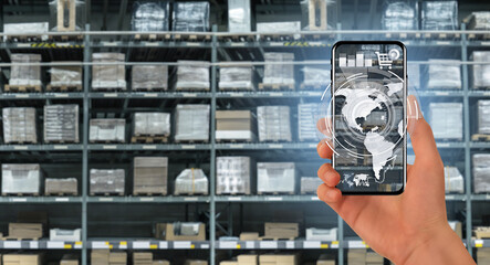 Poster - Hand with a phone on the background of a warehouse. Online trade and logistics concept