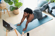 © Alessandro Biascioli - Young African curvy woman doing pilates virtual fitness class with laptop at home - Sport wellness people lifestyle concept
