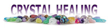 Crystal Healing Tumbled Stones Banner - Wide Selection Of Tumbled Healing Stones Laid In A Neat Row Isolated On White With Two Words Rising Up CRYSTAL HEALING In Purple
