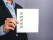 © meeboonstudio - Midsection of a businessman holding a white paper with a checklist against a gray background