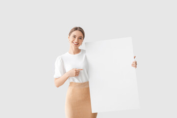 Beautiful young woman with blank poster on light background