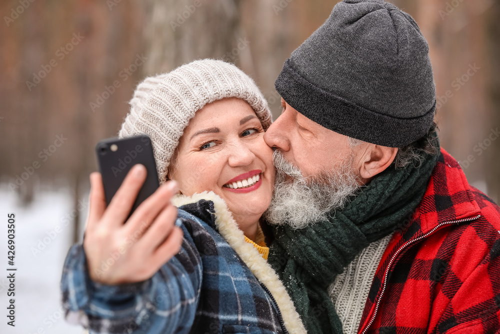 Happy mature couple taking selfie in forest on winter day
