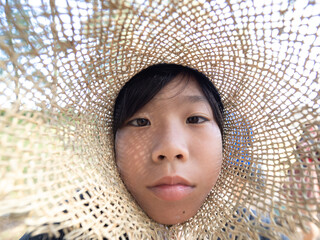 Portrait of a cute little asian boy in a straw hat,  He looks into the frame. Selective focus