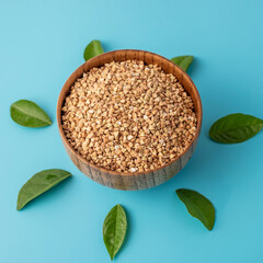 Wooden bowl of green buckwheat with leaves around it on the blue background. Concept of proper balanced nutrition and healthy food