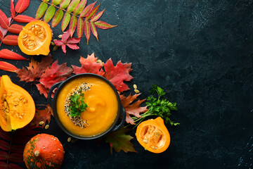 Wall Mural - Pumpkin soup with pumpkin and colored autumn leaves. flat lay. On a black stone background. Top view. Free space for your text.