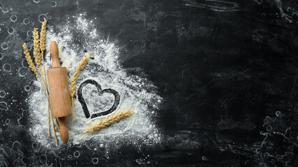 Wall Mural - Wooden rolling pin and flour. Bakery on a black stone background. Top view. Free space for text.