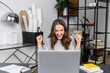 Got it. Excited young woman in casual wear scream yes sitting in front of a laptop in modern office, female employee celebrate best deal, job offer, win in online lottery, raising arms happily