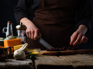 Wall Mural - Chef cuts blackberries for cooking meat or salad on the background of ingredients.Various cheeses, garlic, tomatoes and spices.Culinary recipes