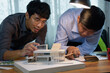 © kokliang1981 - Asian architects discussing with designer or civil engineer about concept of building design and construction project for modern box house. Focusing on the house model.