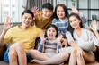 family portrait asian multi gneration parent grandparent and grandchild sit relax together smile hand wave to say hi look at camera on sofa at living room home interior background