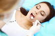© rogerphoto - Young female patient visiting dentist office.Beautiful woman with healthy straight white teeth sitting at dental chair with open mouth during oral checkup while doctor working at teeth