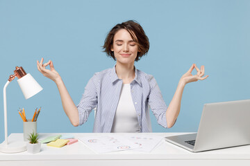 Young successful employee business woman in casual shirt sit work at white office desk with pc laptop hold hands in yoga om gesture relax meditate try to calm down isolated on blue background studio