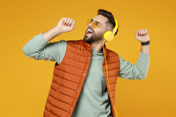 Wall Mural - Young joyful happy cheerful fun caucasian man 20s years old wear orange vest mint sweatshirt glasses headphones singing song in microphone dancing isolated on yellow color background studio portrait