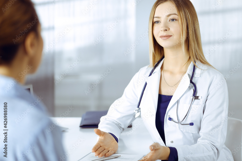 Young intelligent woman-doctor is talking with a smile to her patient ...