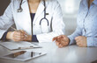 © rogerphoto - Unknown woman- doctor is listening to her patient, while sitting together at the desk in the cabinet in a clinic. Female physician with a stethoscope is writing at clipboard, close up. Perfect medical