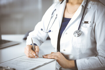 Wall Mural - Unknown woman-doctor is prescribing some medication for her patient, using a clipboard, while sitting at the desk in her cabinet. Female physician with a stethoscope, close up. Perfect medical service