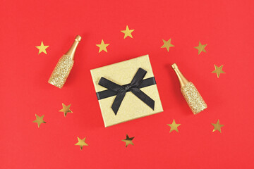 Wall Mural - Golden gift box with black bow, small Champagne bottles and stars on red background