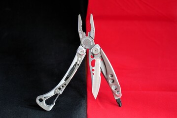 Folding multi tool with stainless steel sharp blade silver handle carabineer and screwdriver closeup still life black red background