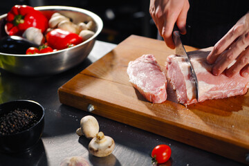 Wall Mural - The male chef cuts raw meat with a knife on a wooden board. The restaurant kitchen cooking.