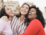 Fototapeta  - Happy latin women laughing and hugging each other outdoor in the city - Millennial girls and friendship concept