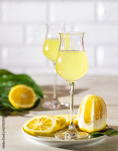Obraz Dibond Limoncello, traditional Italian liquor on a light concrete background in the rays of the sun. Next to it is a yellow lemon, fresh citrus fruits.