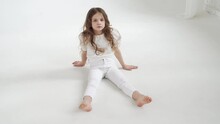 Beautiful Little Girl With Long Hair In White Clothes Sits On The Floor.