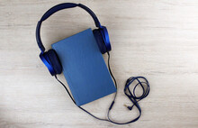 Blue Book With Blue Wired Headphones On A Wooden Background. Audiobook Concept