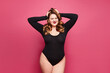 Beautiful emotional plus-size female model in a black bodysuit posing on pink background in studio