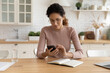 © fizkes - Confident young hispanic female work from home sit at desk search information online using internet resources via phone. Young woman freelancer texting client set up business meeting at suitable time