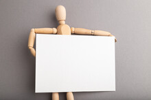 Wooden Mannequin Holding Blank Poster On Gray Pastel Background. Copy Space.