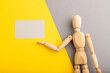 Wooden mannequin holding gray blank poster on gray and yellow pastel background. copy space.