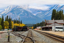 Railway Tracks In Small Mountain Town Surrounded By Massive Mountains In The Clouds On Autumn Day With Colourful Trees