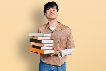 Poster - Handsome hipster young man holding a pile of books looking at the camera blowing a kiss being lovely and sexy. love expression.