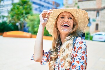 Poster - Young beautiful blonde woman on vacation wearing summer hat smiling happy. Standing with smile on face at street of city.