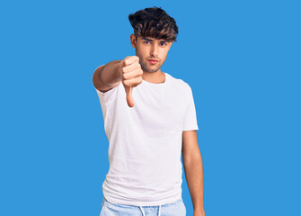 Wall Mural - Young hispanic man wearing casual clothes looking unhappy and angry showing rejection and negative with thumbs down gesture. bad expression.