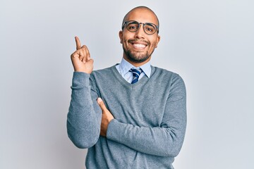 Wall Mural - Hispanic adult man wearing glasses and business style with a big smile on face, pointing with hand and finger to the side looking at the camera.