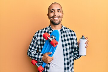 Wall Mural - Hispanic adult skater man holding skate and graffiti spray smiling with a happy and cool smile on face. showing teeth.