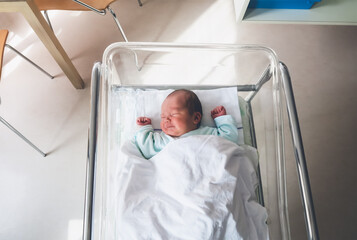 newborn baby is sleeping in small transparent portable plastic bed. baby first days of life is lying