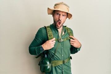 Poster - Handsome man with beard wearing explorer hat and backpack in shock face, looking skeptical and sarcastic, surprised with open mouth