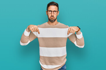 Sticker - Handsome man with beard wearing casual clothes and glasses pointing down looking sad and upset, indicating direction with fingers, unhappy and depressed.