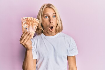 Sticker - Caucasian young man with long hair holding 20 philippine peso banknotes scared and amazed with open mouth for surprise, disbelief face