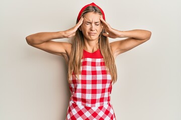 Wall Mural - Young blonde woman wearing professional baker apron with hand on head, headache because stress. suffering migraine.