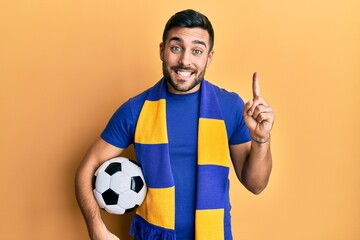 Wall Mural - Young hispanic man football hooligan soccer ball smiling with an idea or question pointing finger with happy face, number one