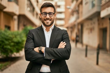 Poster - Young hispanic businessman with arms crossed smiling happy at the city.