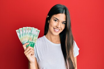 Poster - Young brunette woman holding hong kong 50 dollars banknotes looking positive and happy standing and smiling with a confident smile showing teeth