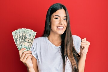 Canvas Print - Young brunette woman holding 20 dollars banknote screaming proud, celebrating victory and success very excited with raised arm