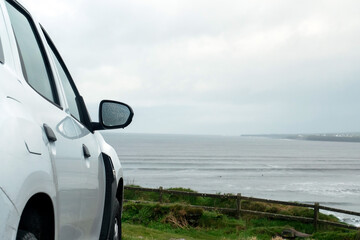 Wall Mural - Side of a white car parked with view on beautiful ocean scene. Travel and rent vehicle concept