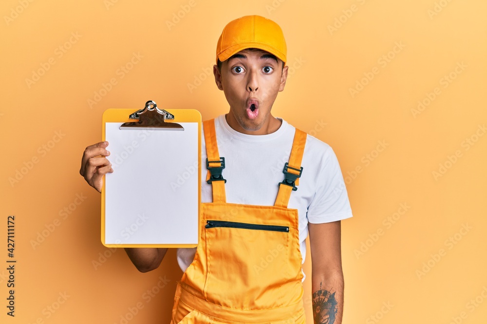 Young handsome african american man wearing courier uniform holding clipboard scared and amazed with open mouth for surprise, disbelief face